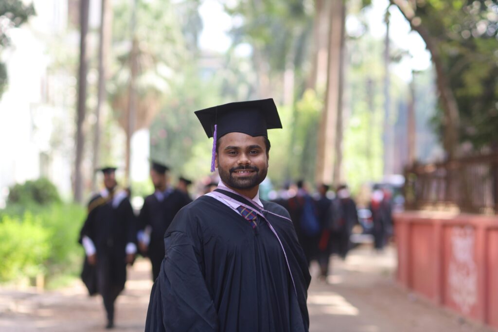 Graduate in cap and gown smiling proudly outdoors, symbolizing achievement and education.