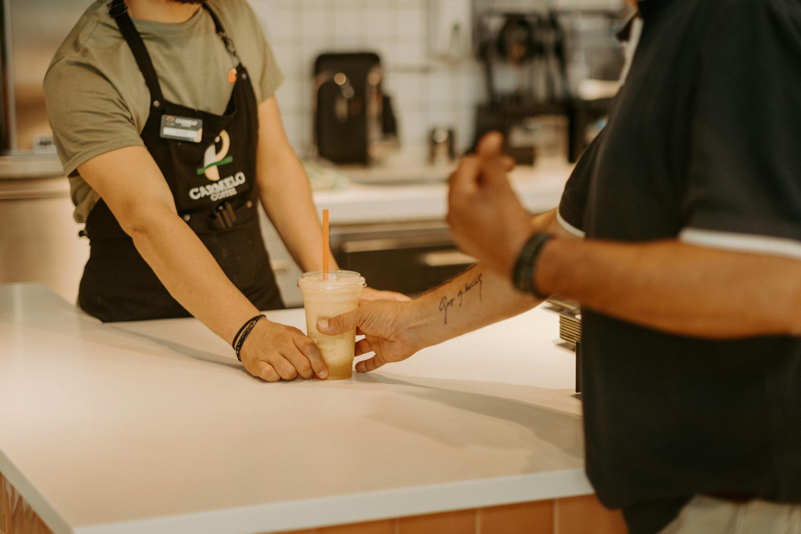 Barista hands cold drink to customer in cozy café setting, showcasing hospitality.